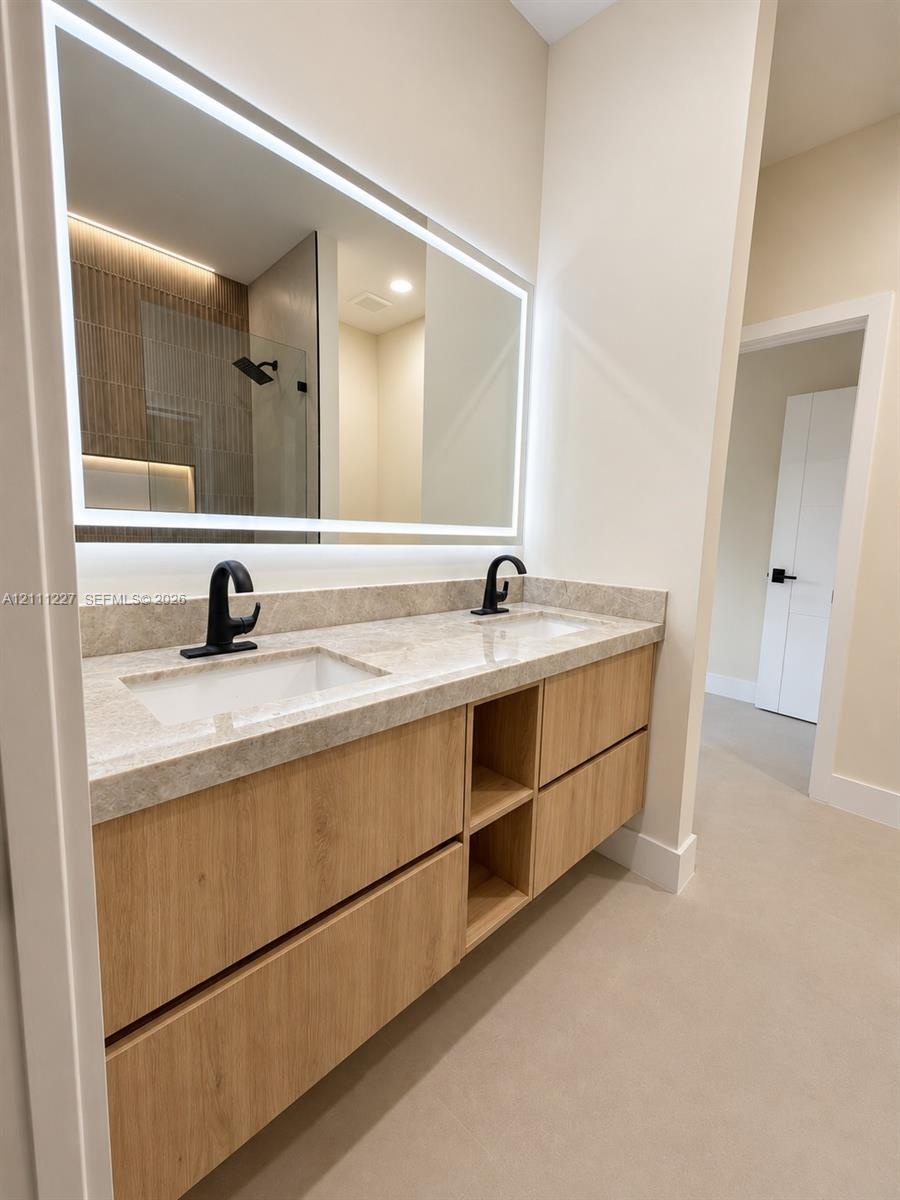 Double vanity featuring light wood-finish cabinetry with open shelving, stone countertop, matte black fixtures, and a large LED-backlit mirror