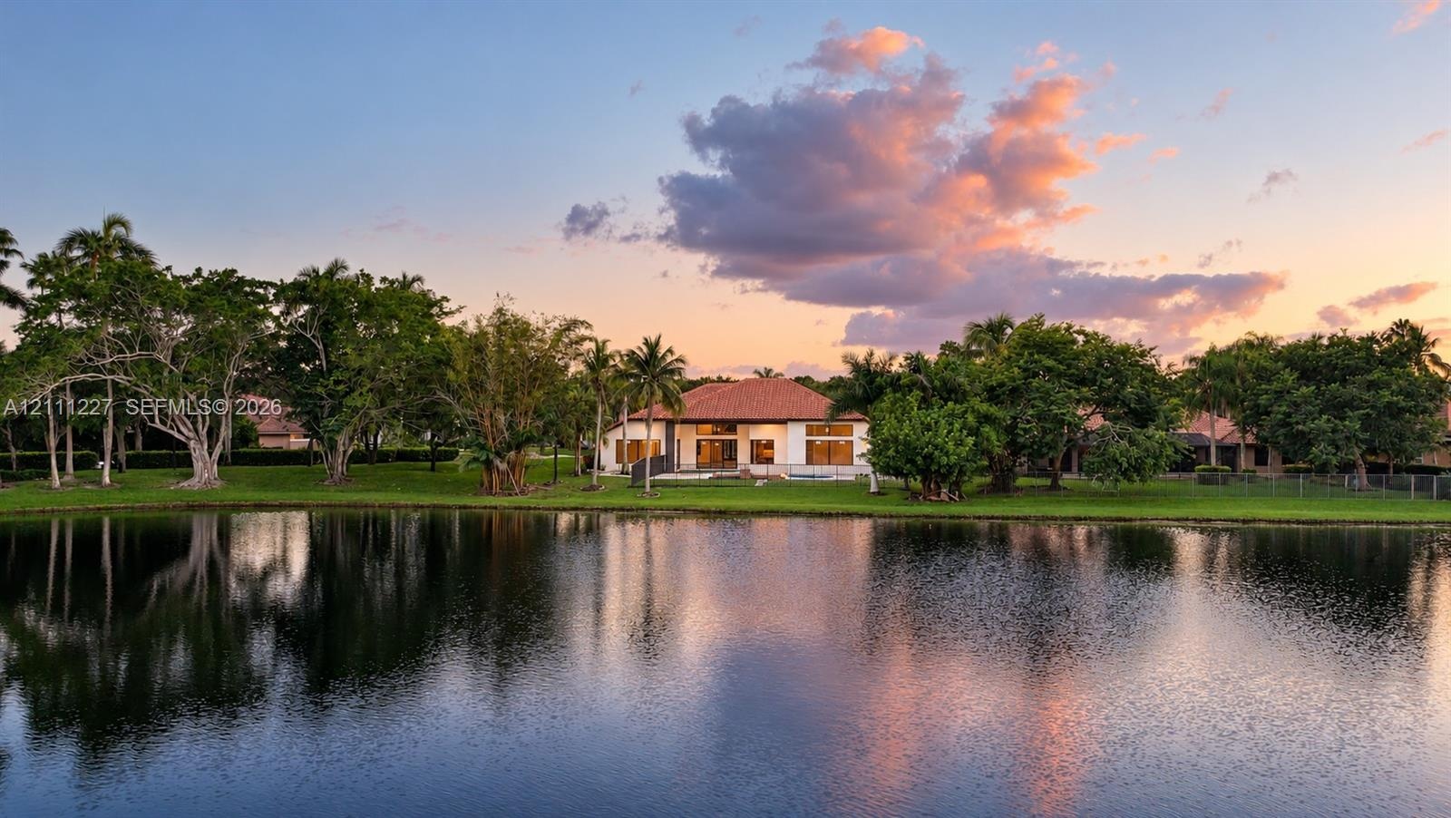 Waterfront residence featuring a tile roof, expansive lawn, mature landscaping, and palm trees