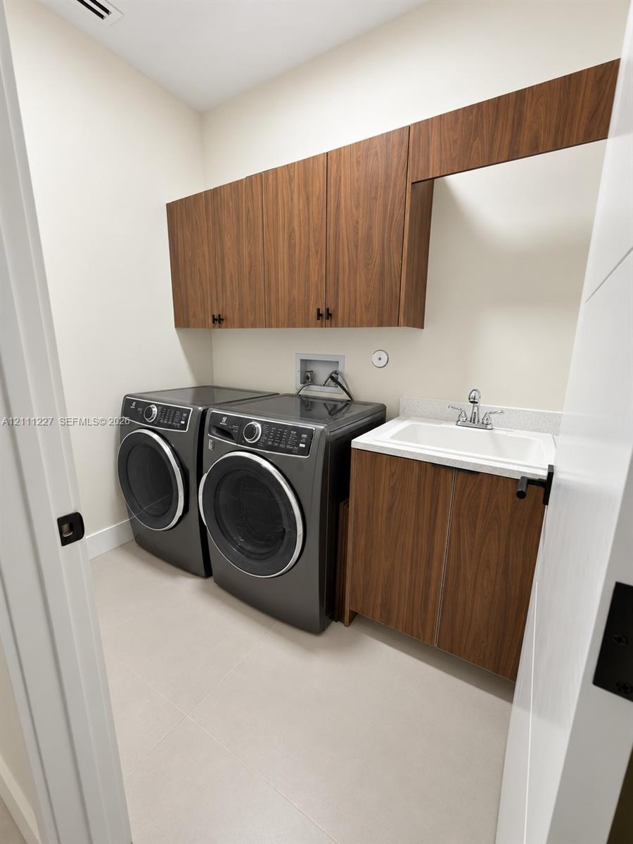 Utility room featuring wood-finish cabinetry, a built-in sink with a stone-surfaced countertop, and neutral tile flooring