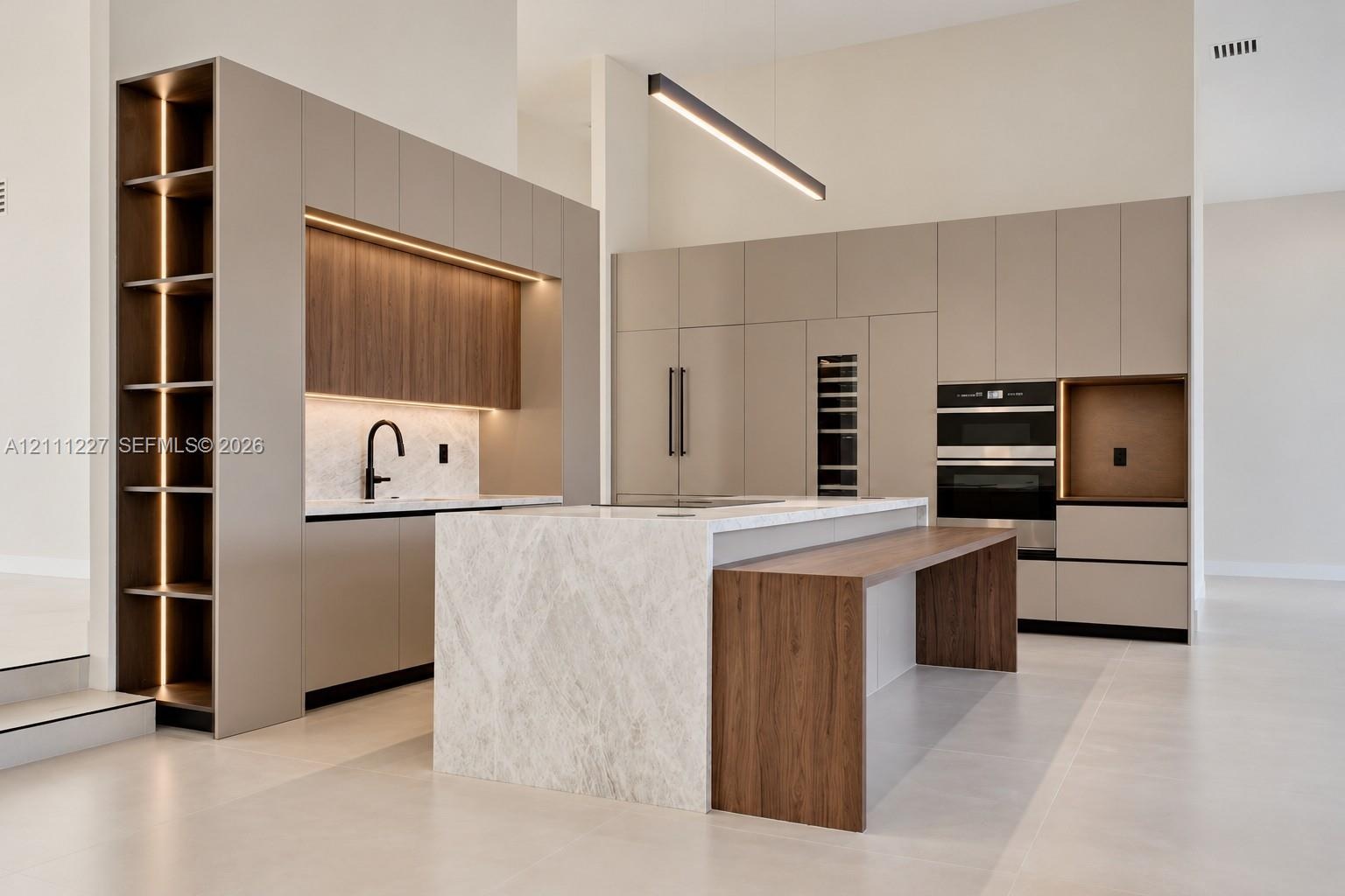 Modern kitchen featuring flat-panel cabinetry, a waterfall-edge stone island with an integrated wood-finish breakfast bar, built-in double ovens, and 