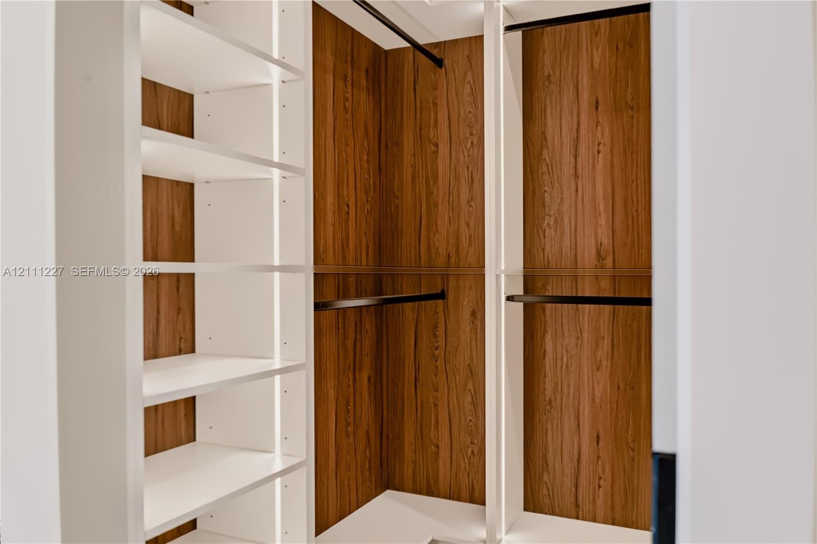 Custom walk-in closet featuring white open shelving, wood-finish paneling, and matte black hanging rods
