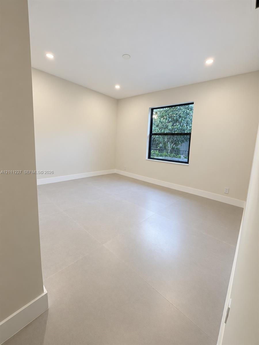 Interior space featuring large-format tile flooring, neutral wall tones, recessed lighting, and a window with a black frame