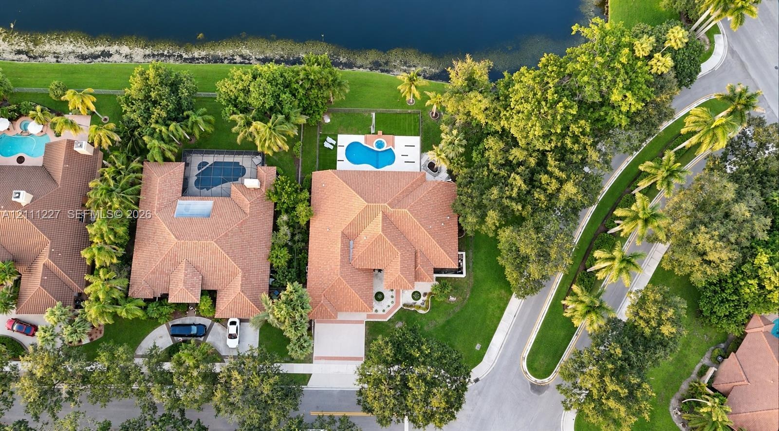 Aerial view of a waterfront property featuring a multi-hipped tile roof, a private swimming pool with a concrete patio, and mature landscaping