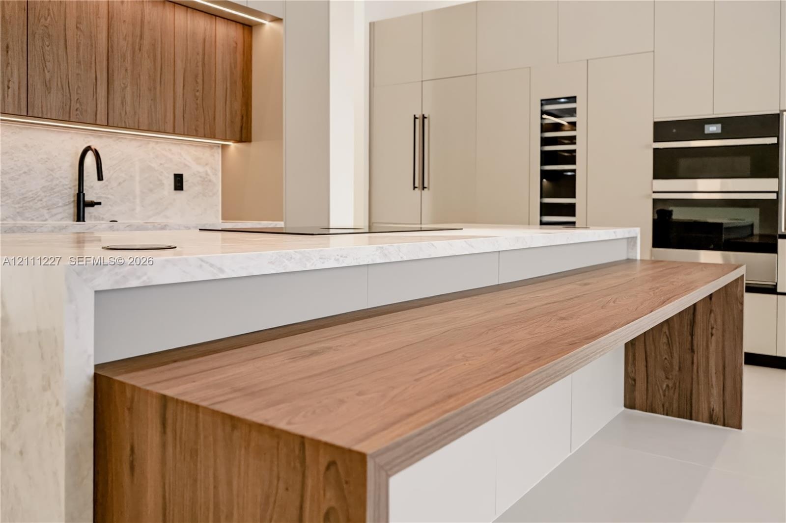 Kitchen featuring a waterfall-edge island with wood-finish counter seating, integrated stainless steel appliances, full-height cabinetry, stone-finish