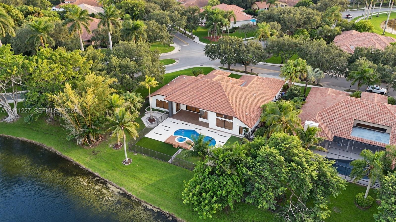 Aerial perspective of a single-story residence featuring a tile roof, a rear patio with an inset swimming pool and spa, and expansive lawn space with 