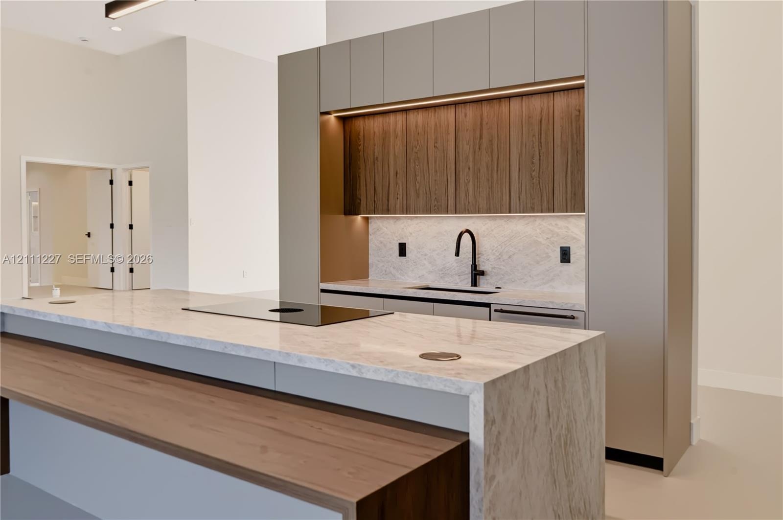 Modern kitchen featuring full-height flat-panel cabinetry, a wood-finish recessed upper cabinet section with integrated under-cabinet lighting, a wate