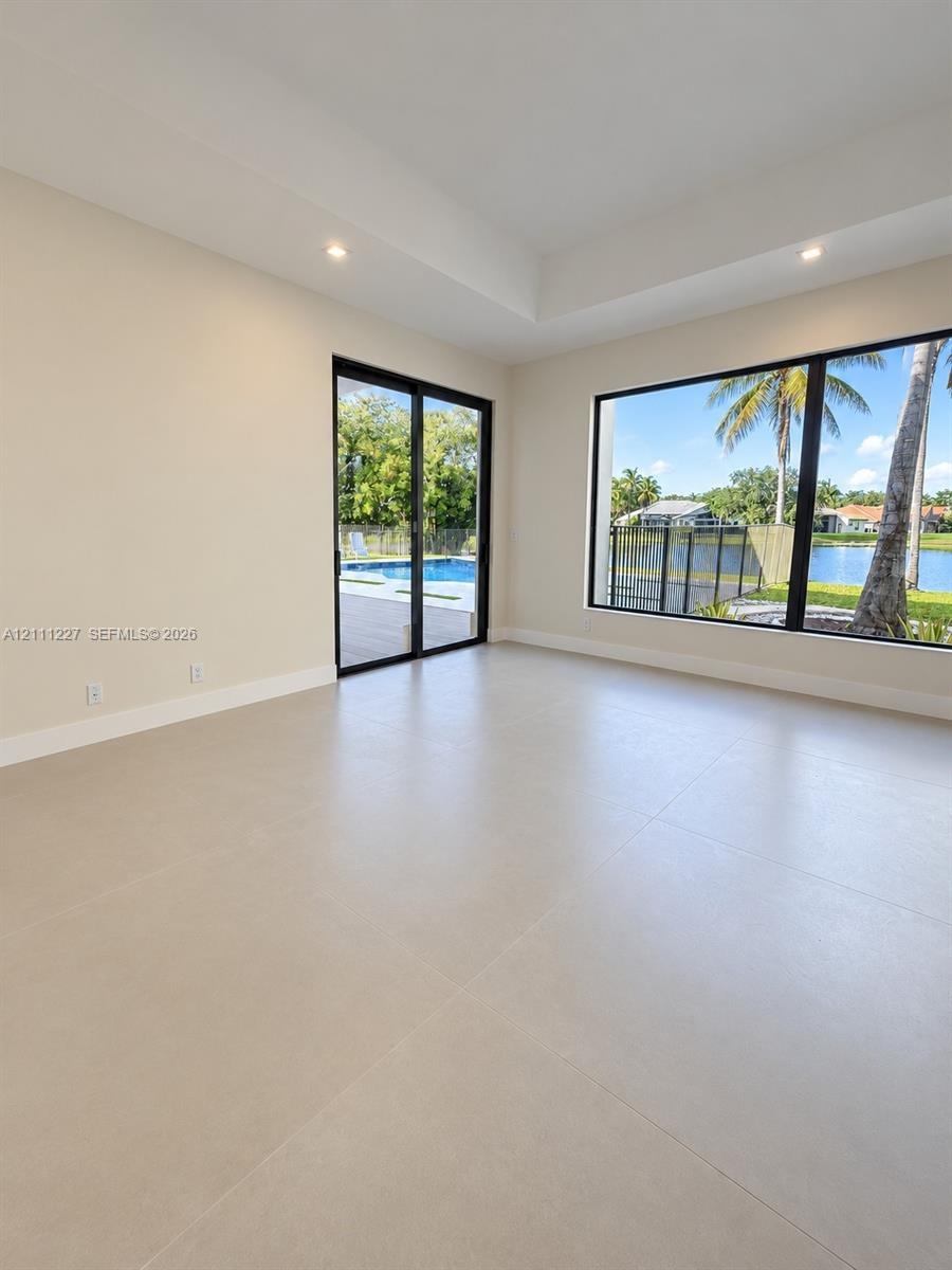 Interior space featuring large-format tile flooring, a tray ceiling with recessed lighting, black-framed picture windows, and sliding glass doors with