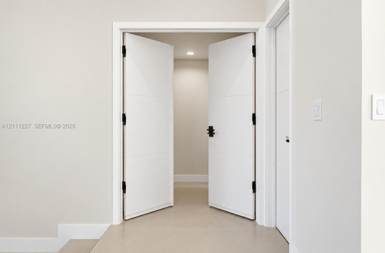 Double doors featuring horizontal panel detailing, matte black hinges, and matte black hardware, offset by neutral walls and light-toned flooring