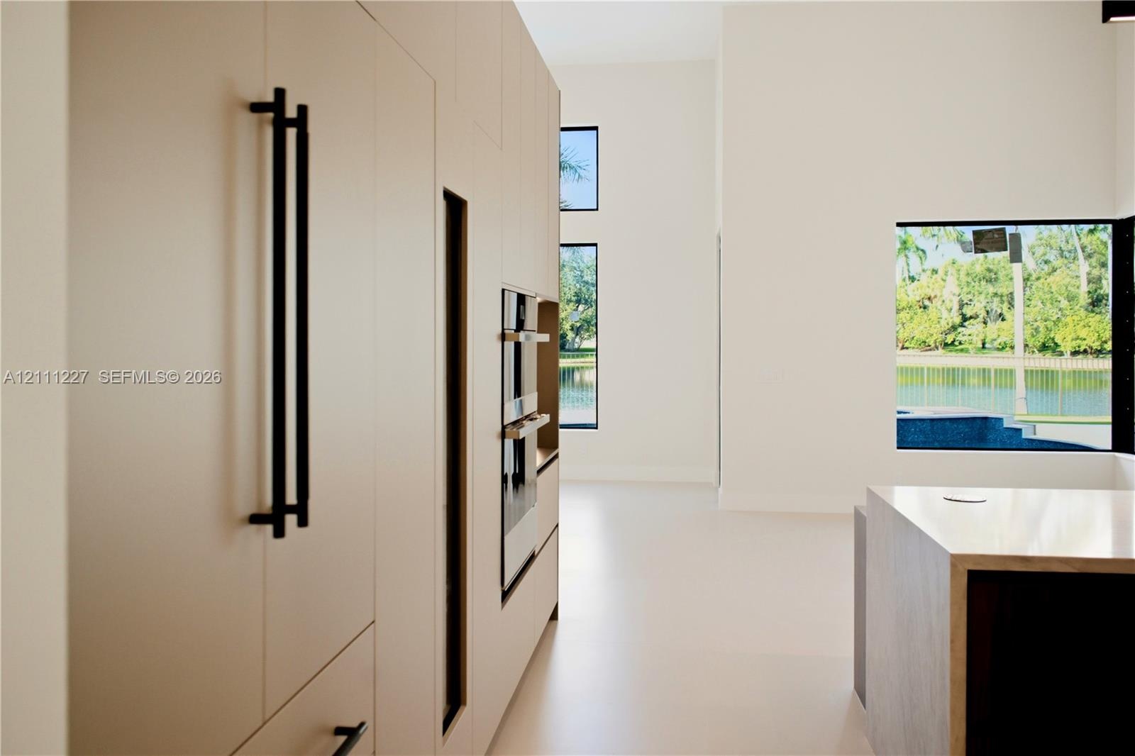 Full-height, flat-panel cabinetry featuring matte black hardware, integrated double wall ovens, expansive floor-to-ceiling windows, and a waterfall-ed