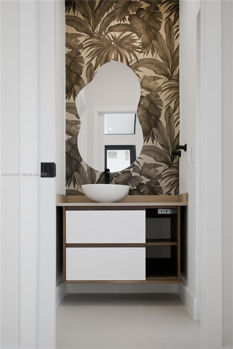 Floating vanity with a white vessel sink, matte black wall-mounted faucet, organic-shaped mirror, and patterned wall covering