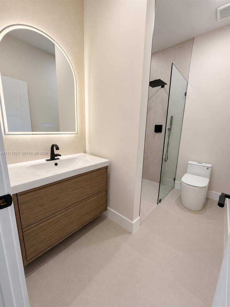 Floating vanity with wood-finish cabinetry, arched LED-backlit mirror, matte black faucet, and walk-in shower with glass panel