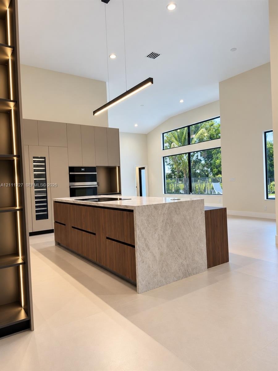 Kitchen featuring a central island with a stone-finish waterfall countertop, built-in dual wall ovens, integrated wine refrigeration, linear pendant l