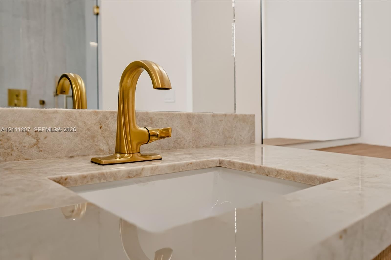 Stone countertop with integrated undermount sink, brushed brass faucet, and tall wall-mounted mirror