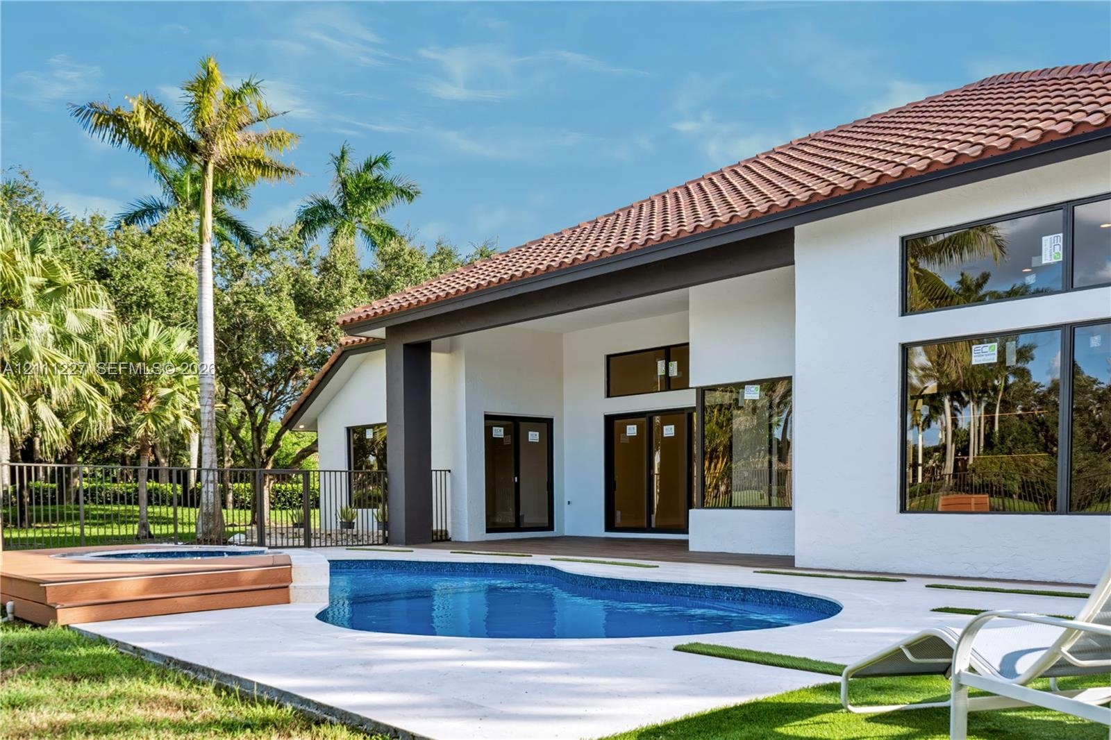 Stucco exterior featuring a tiled roof, covered patio, swimming pool with a raised spa, and large pane windows