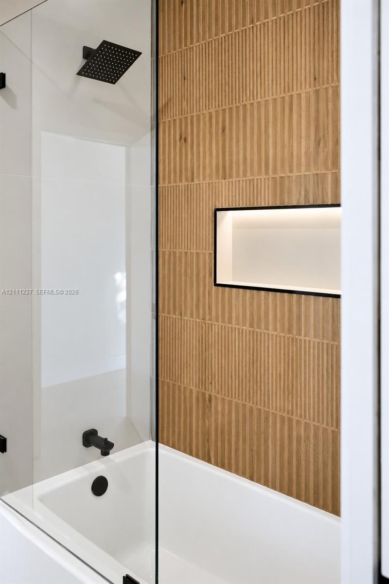 Walk-in shower enclosure featuring floor-to-ceiling vertically textured tile, a built-in recessed niche, a matte black rainfall shower head, and match