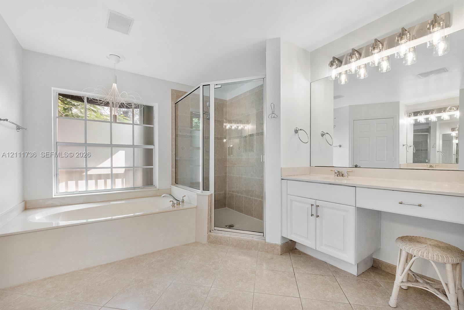 Bathroom featuring a built-in soaking tub, a tiled glass-enclosed shower, dual-basin vanity with solid-surface countertops, and large wall-mounted mir