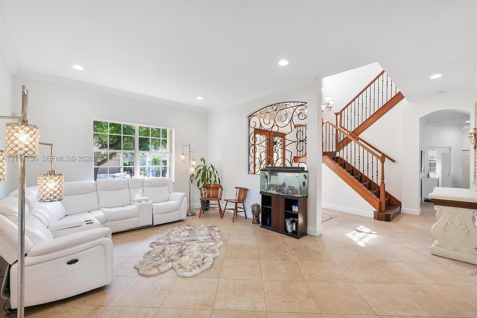 Open-concept area featuring ceramic tile flooring, recessed lighting, ornate wrought iron wall detailing, and a wood staircase with decorative baluste