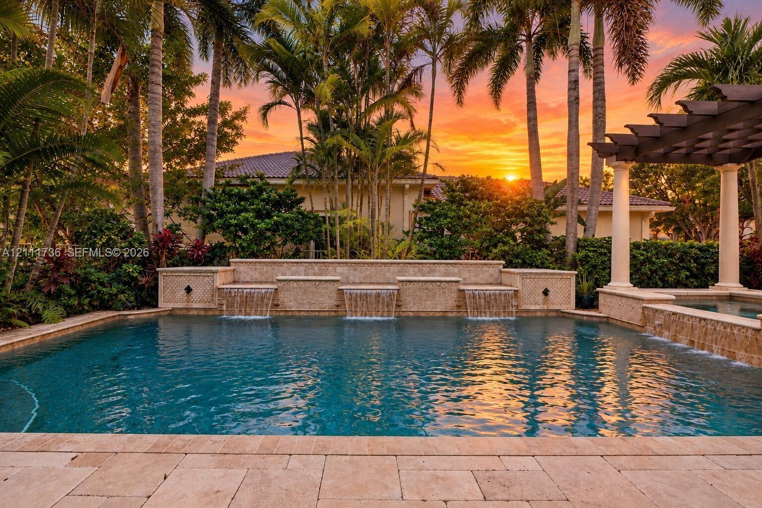 Swimming pool with three cascading water features, stone coping, attached spillover spa, and a pergola structure with decorative columns