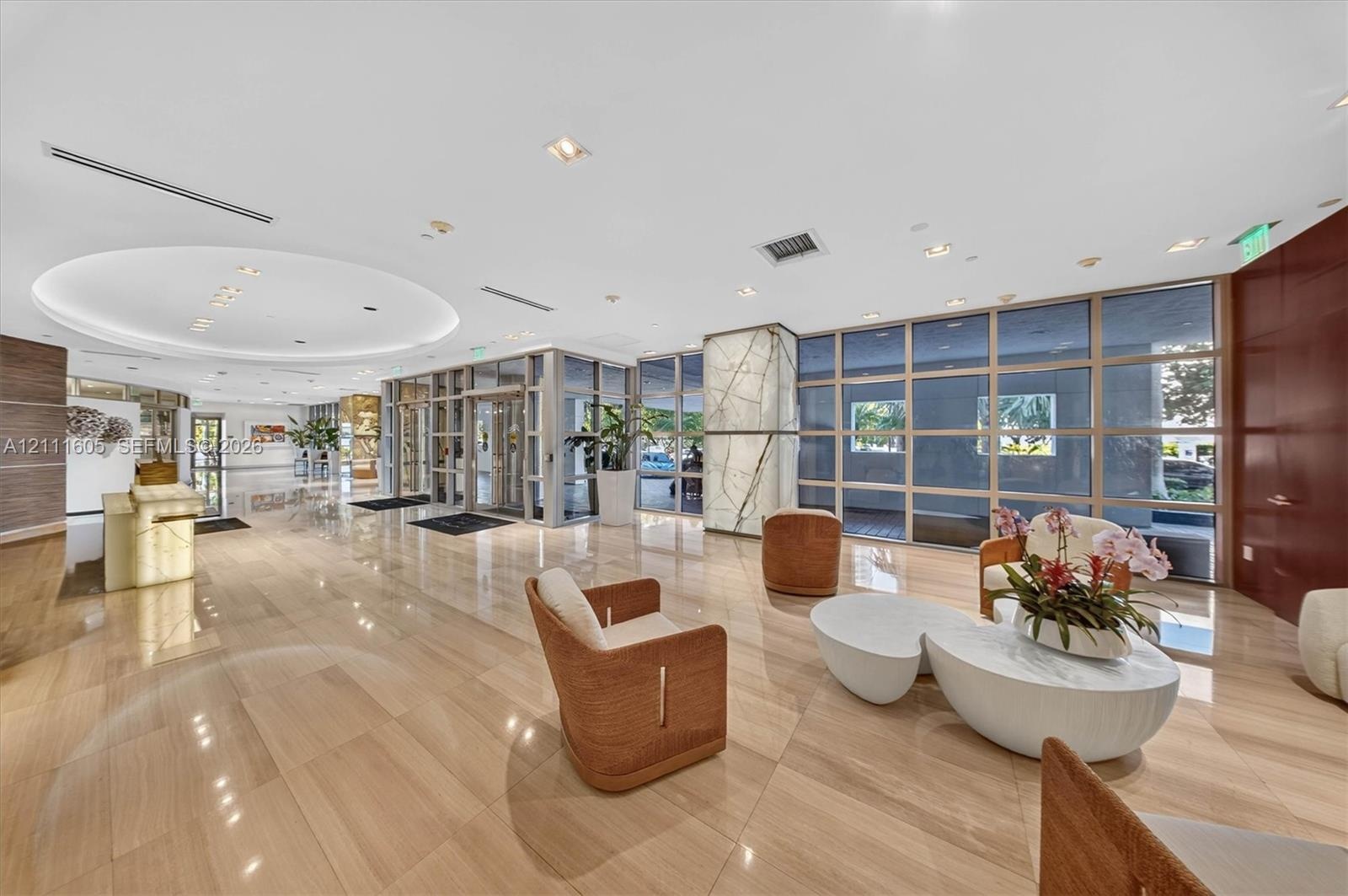 Open-concept living area featuring floor-to-ceiling glass sliding doors, stone-surfaced kitchen island, custom built-in cabinetry, and integrated arch