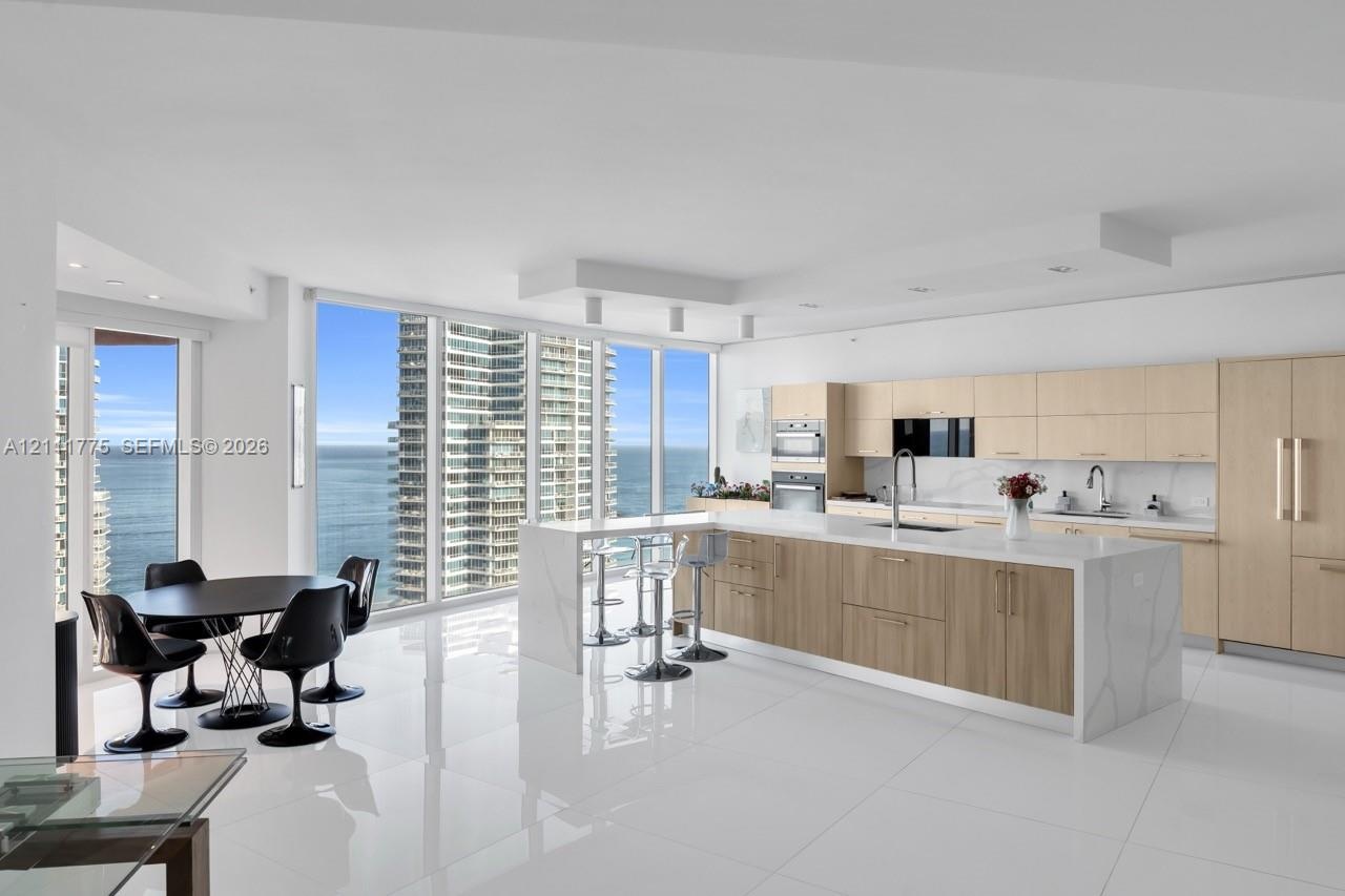 Modern kitchen featuring flat-panel cabinetry, a central island with a stone-finish waterfall countertop, polished tile flooring, and floor-to-ceiling