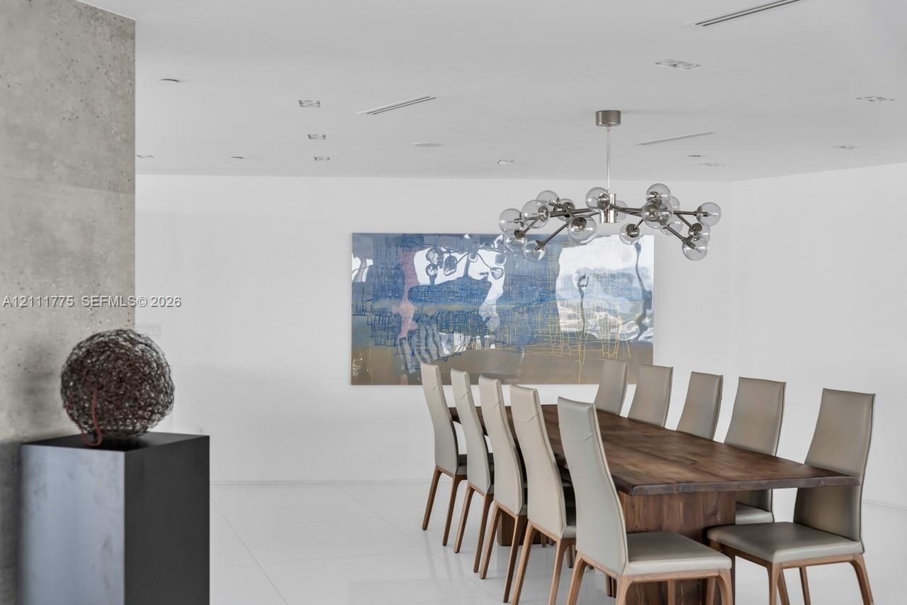 Contemporary living area featuring large-format white tile flooring, a textured concrete-finish accent wall, and a multi-arm modern pendant light fixt