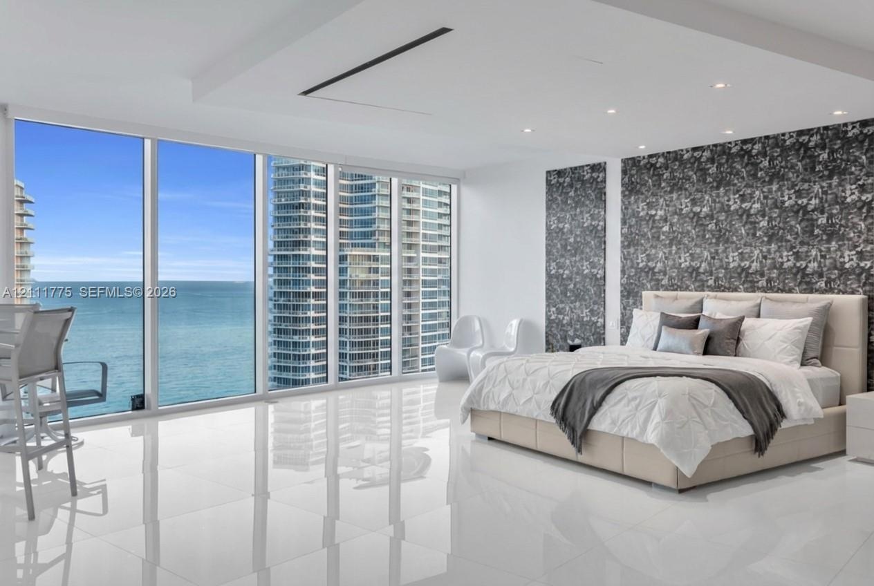 Floor-to-ceiling windows, polished stone-finish flooring, tray ceiling with recessed lighting, and patterned accent wall