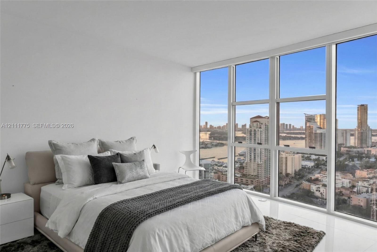 Floor-to-ceiling windows featuring expansive urban and water scenery, white smooth-finish flooring, and white interior wall finishes