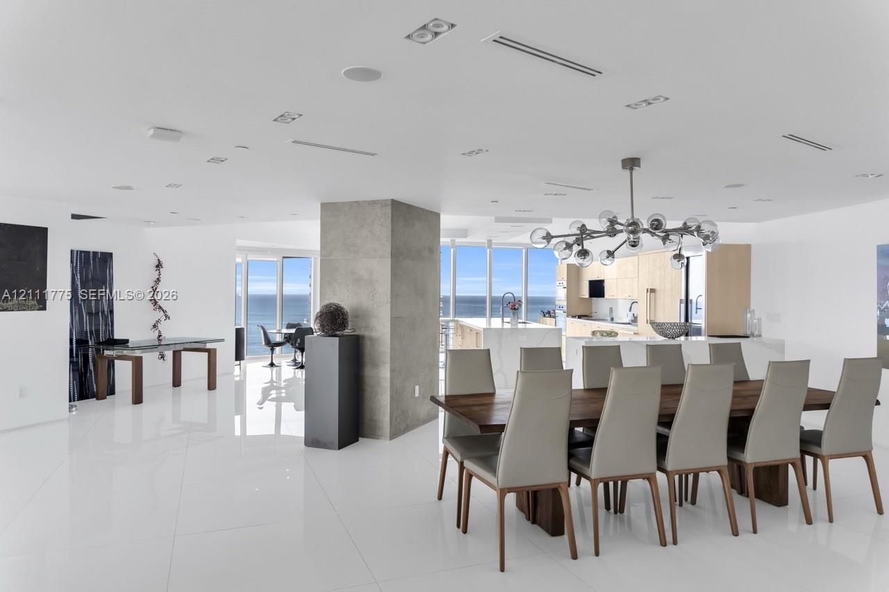 Open-concept interior featuring large-format tile flooring, exposed concrete structural column, recessed lighting, modern multi-globe chandelier, and 