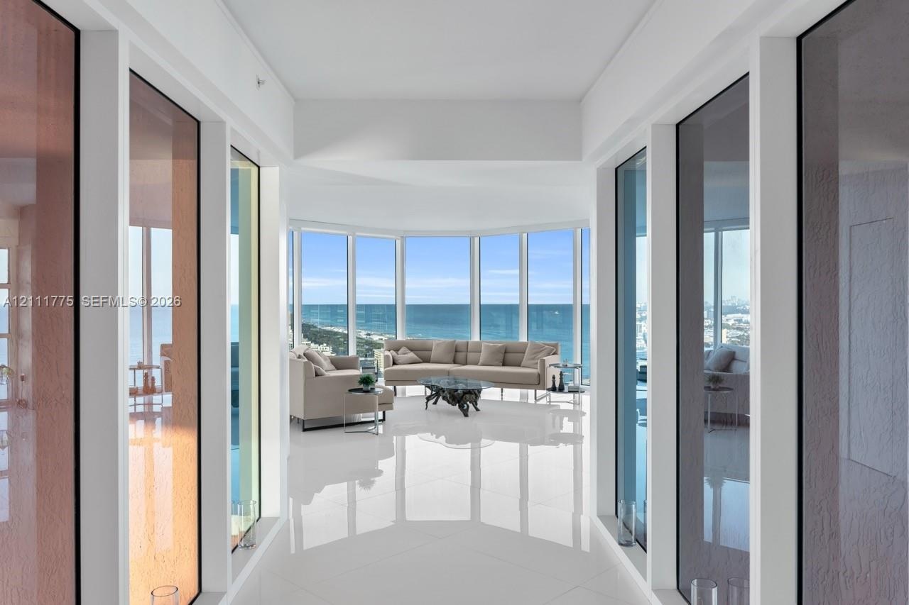 Floor-to-ceiling perimeter windows, polished tile flooring, and expansive water backdrop