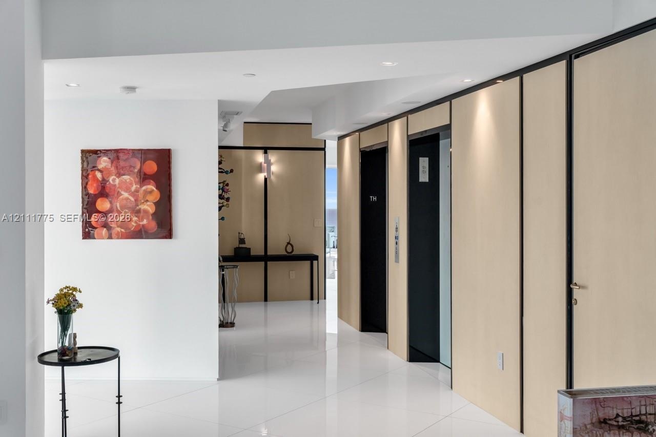 Polished white tile flooring, natural wood-finished wall paneling with black trim, recessed lighting, and integrated elevator access