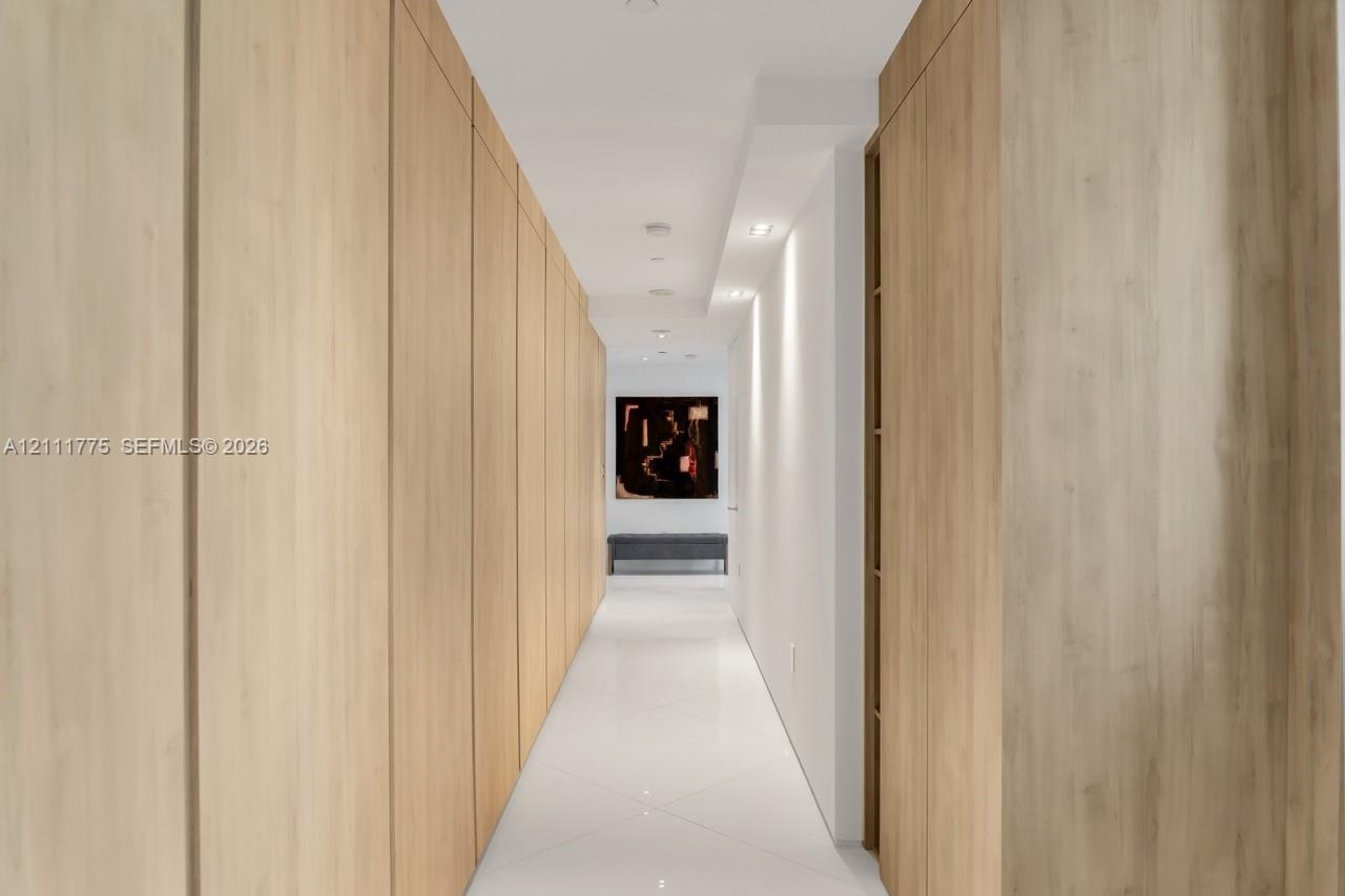 Hallway featuring full-height light wood-finish cabinetry, polished tile flooring, and recessed ceiling lighting