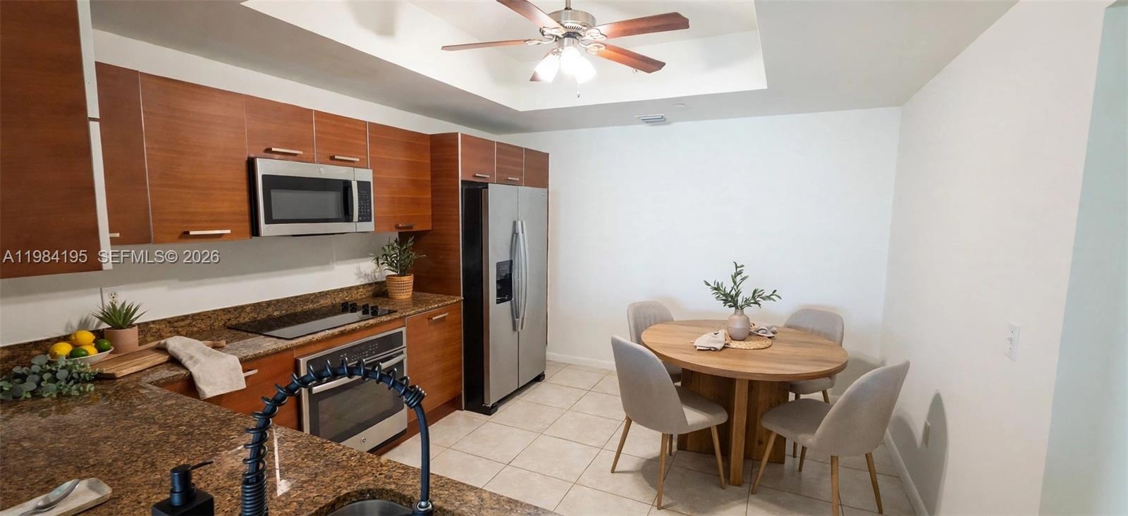 Kitchen featuring wood-finish cabinetry, stone countertops, stainless steel appliances, a tray ceiling, and tile flooring