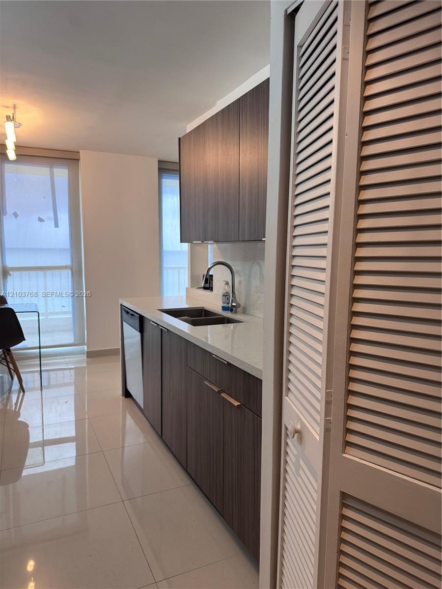 Kitchen featuring flat-panel wood-finish cabinetry, light-toned stone-surface countertops, dual-basin under-mount sink with pull-down faucet, porcelai