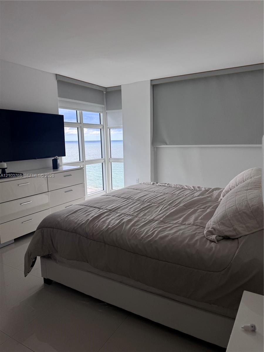 Floor-to-ceiling windows featuring ocean scenery, light-colored tile flooring, and neutral wall tones