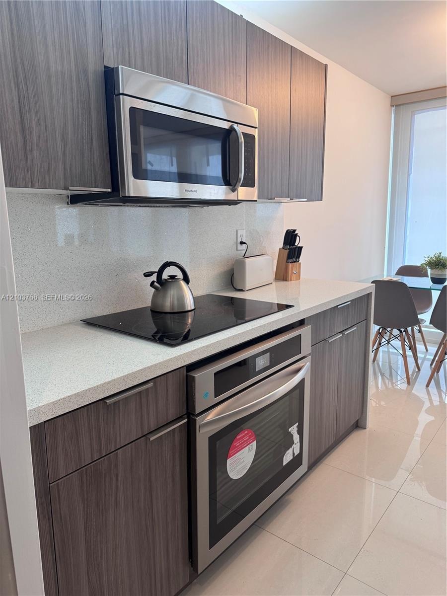 Kitchen featuring flat-panel wood-finish cabinetry, quartz countertops, full-height quartz backsplash, built-in stainless steel oven, and integrated c