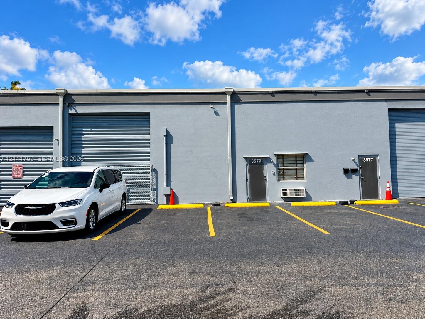 Exterior commercial facade featuring gray concrete construction, multiple metal roll-up bay doors, individual pedestrian entry doors, and dedicated as