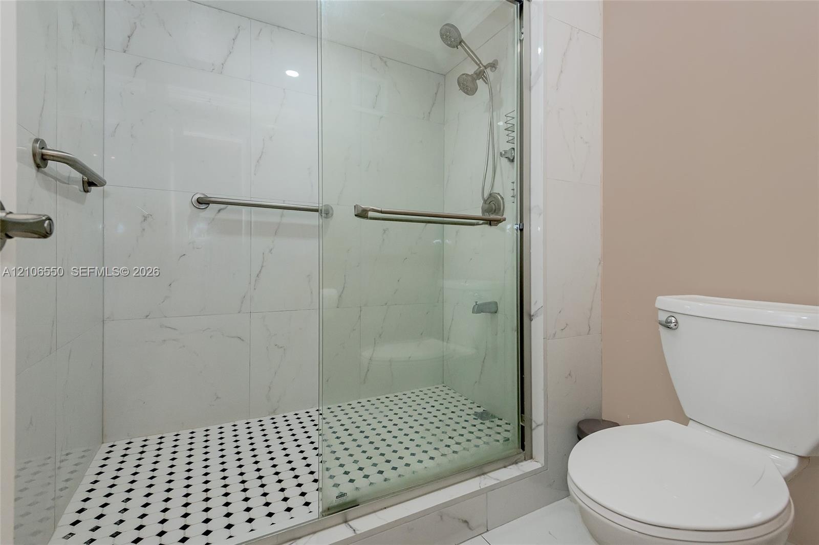 Primary Bathroom. Walk-in shower featuring large-format stone-look wall tiling, a mosaic tile floor, glass sliding doors, and chrome fixtures
