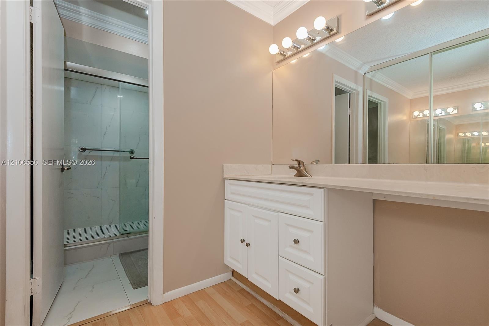 Primary Bathroom vanity featuring a white cabinet base, stone-look countertop, integrated sink, and full-width wall mirror with attached multi-bulb li
