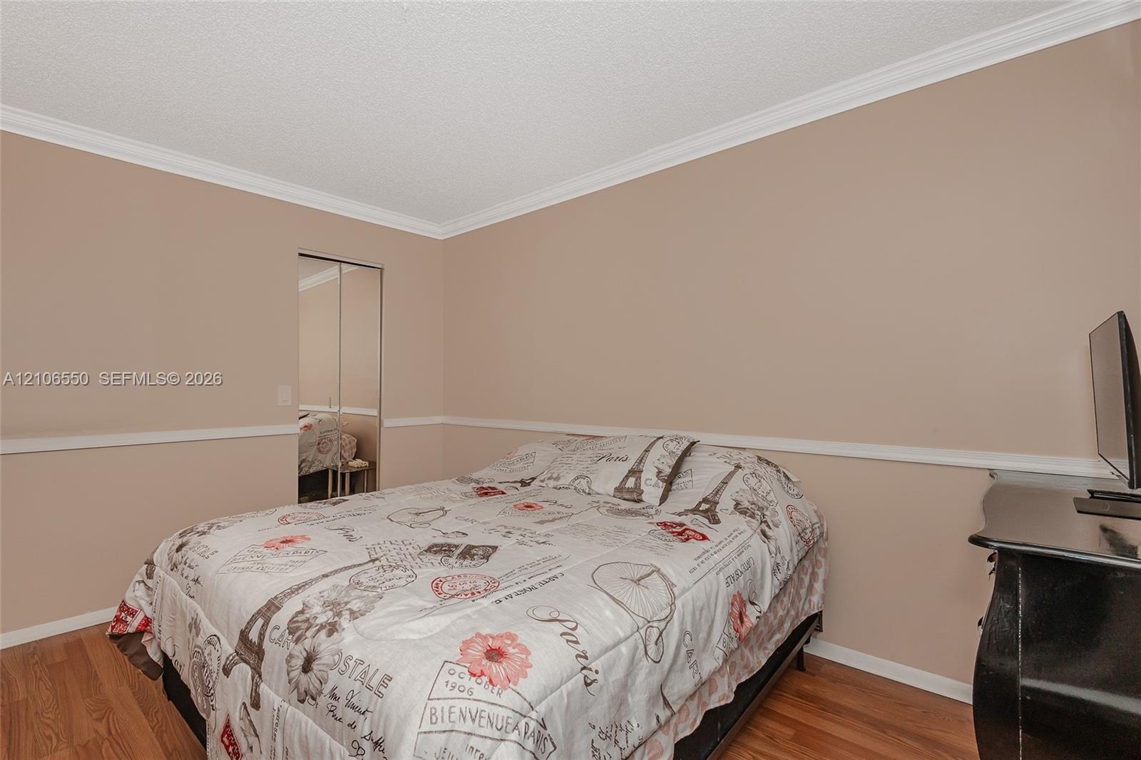 Room featuring wood-finish flooring, crown molding, chair rail trim, and mirrored sliding closet doors
