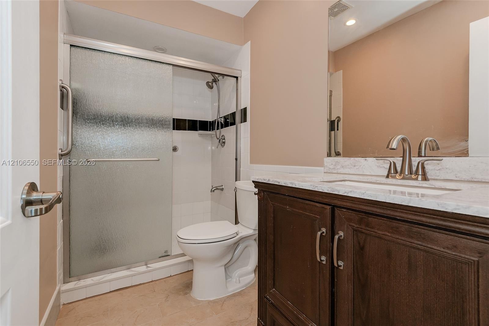 Bathroom featuring a dark wood vanity with a stone-finish countertop, undermount sink, shower with sliding glass doors, and a frameless wall mirror