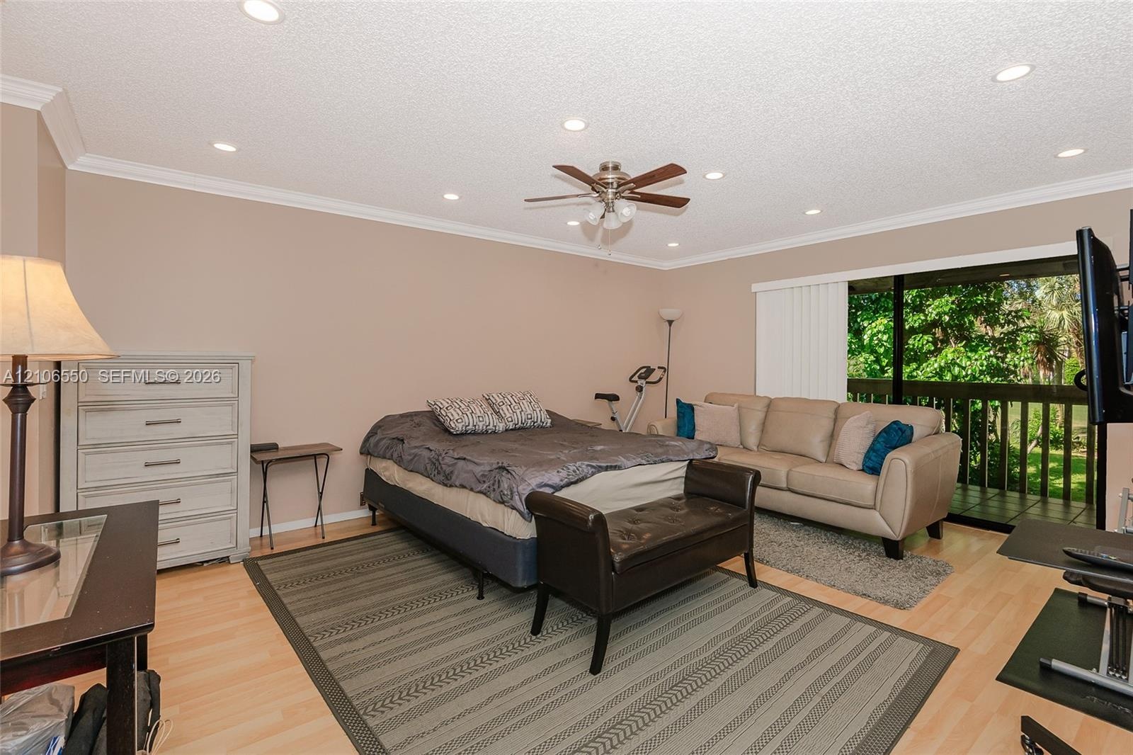 Primary bedroom. Light-toned wood-finish flooring, recessed ceiling lighting, central ceiling fan with integrated light fixture, crown molding, and sl