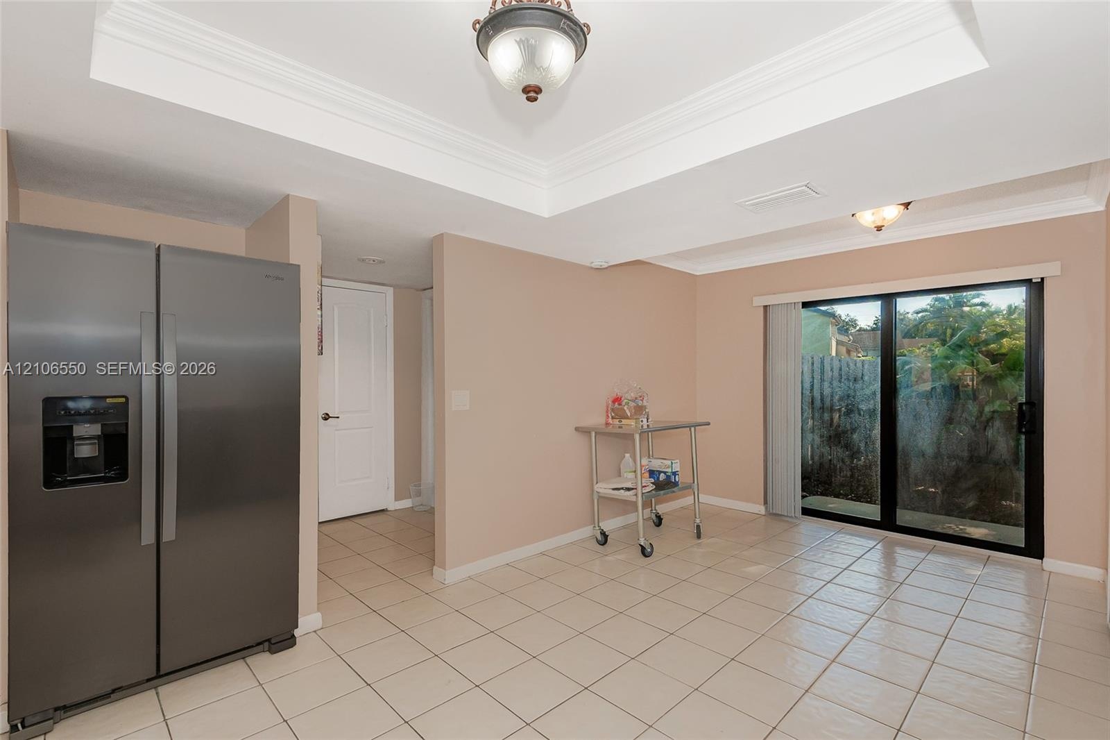 Tray ceiling with crown molding, stainless steel side-by-side refrigerator, ceramic tile flooring, and sliding glass doors