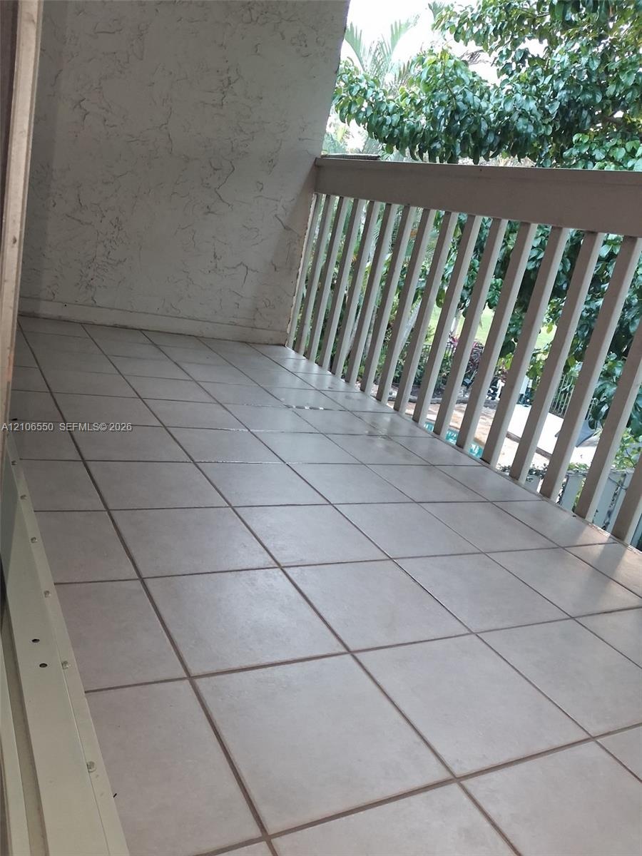 Covered balcony featuring neutral ceramic tile flooring, textured wall finish, and a slatted railing