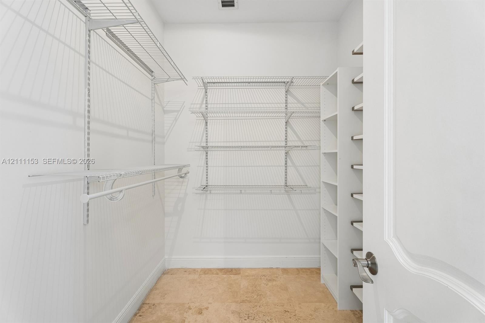 Storage area featuring stone tile flooring, white vertical built-in shelving, and adjustable metal wire rack shelving