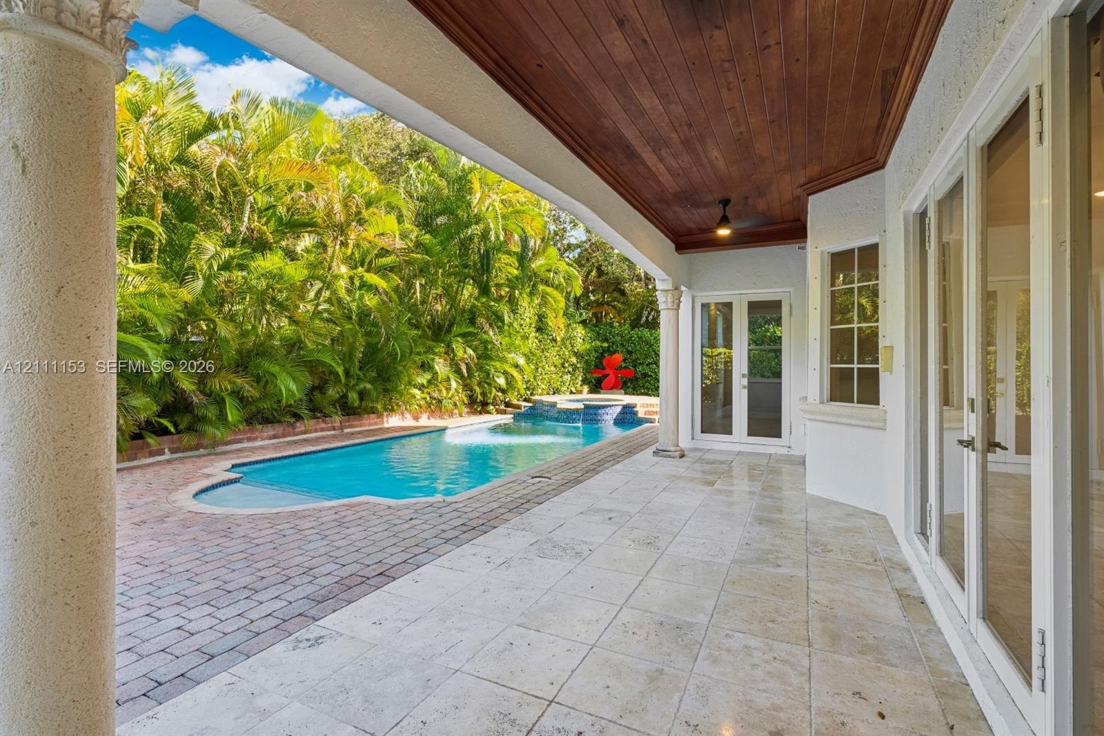 Covered patio featuring a natural wood-plank ceiling, stone tile flooring, and decorative columns