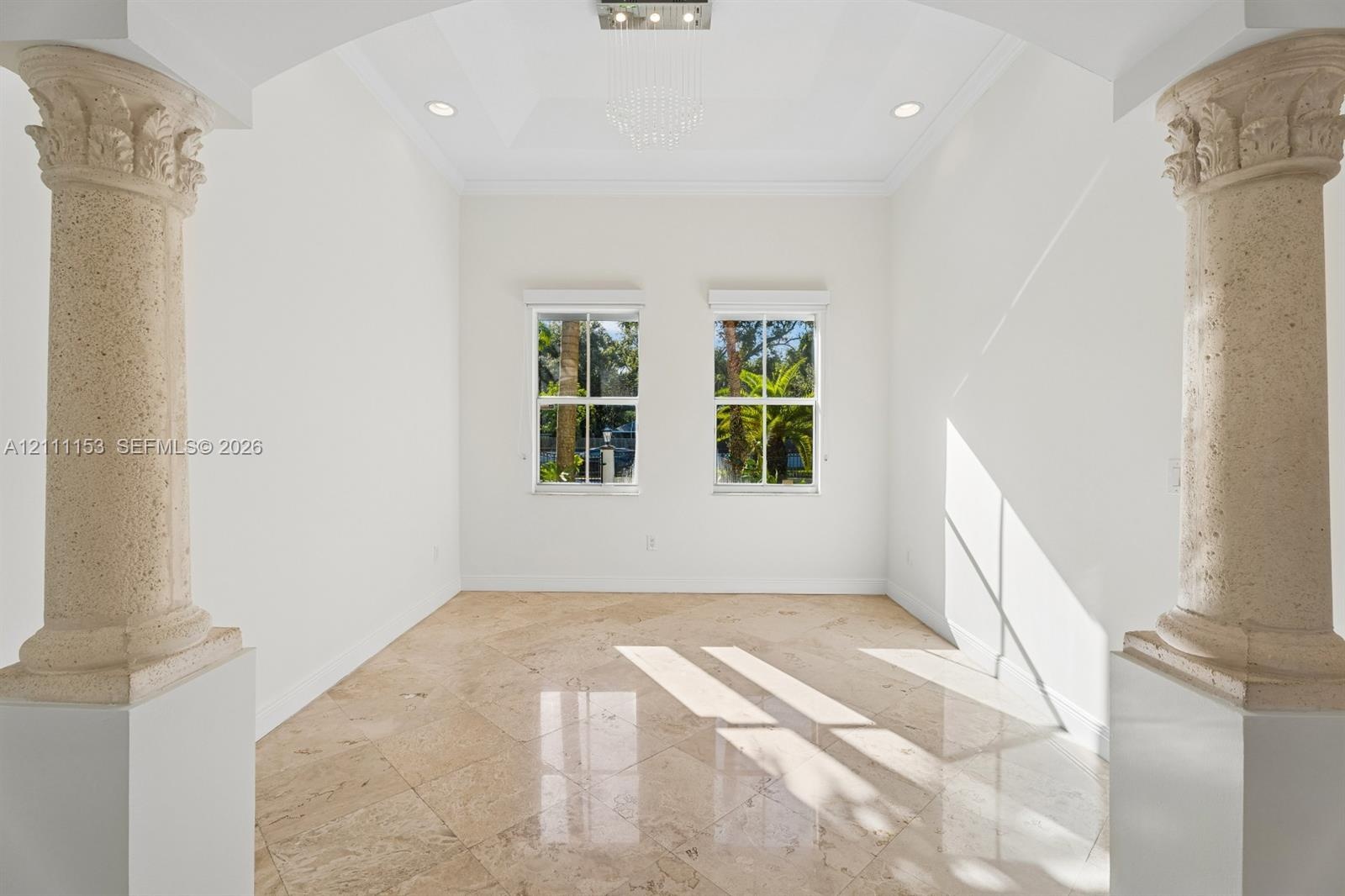 Architectural space defined by decorative stone columns, polished stone flooring, a tray ceiling with recessed lighting, and dual windows