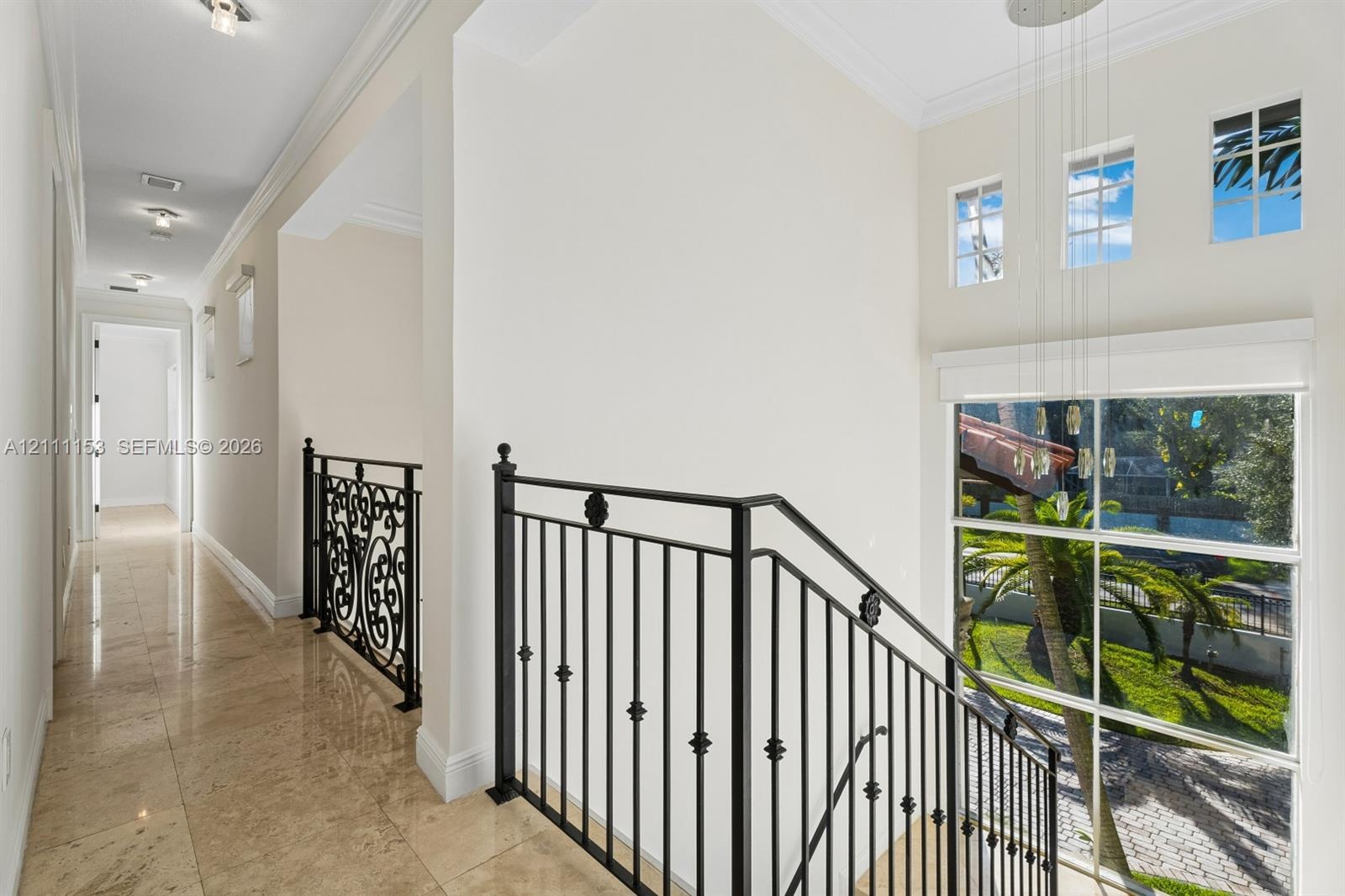 Neutral stone flooring, matte black wrought iron railings with decorative scrollwork, high ceilings, recessed lighting, and large windows featuring mu