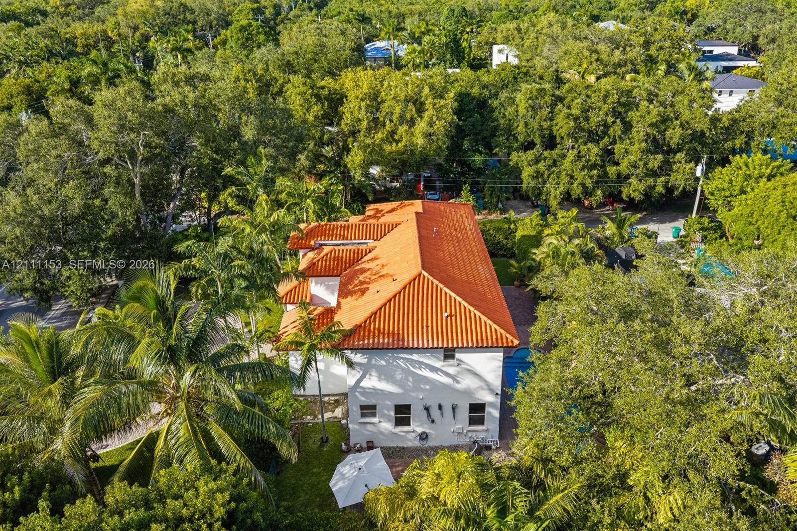 Two-story residence featuring a terracotta-tiled roof, white exterior stucco finish, and an integrated swimming pool situated within a heavily wooded 