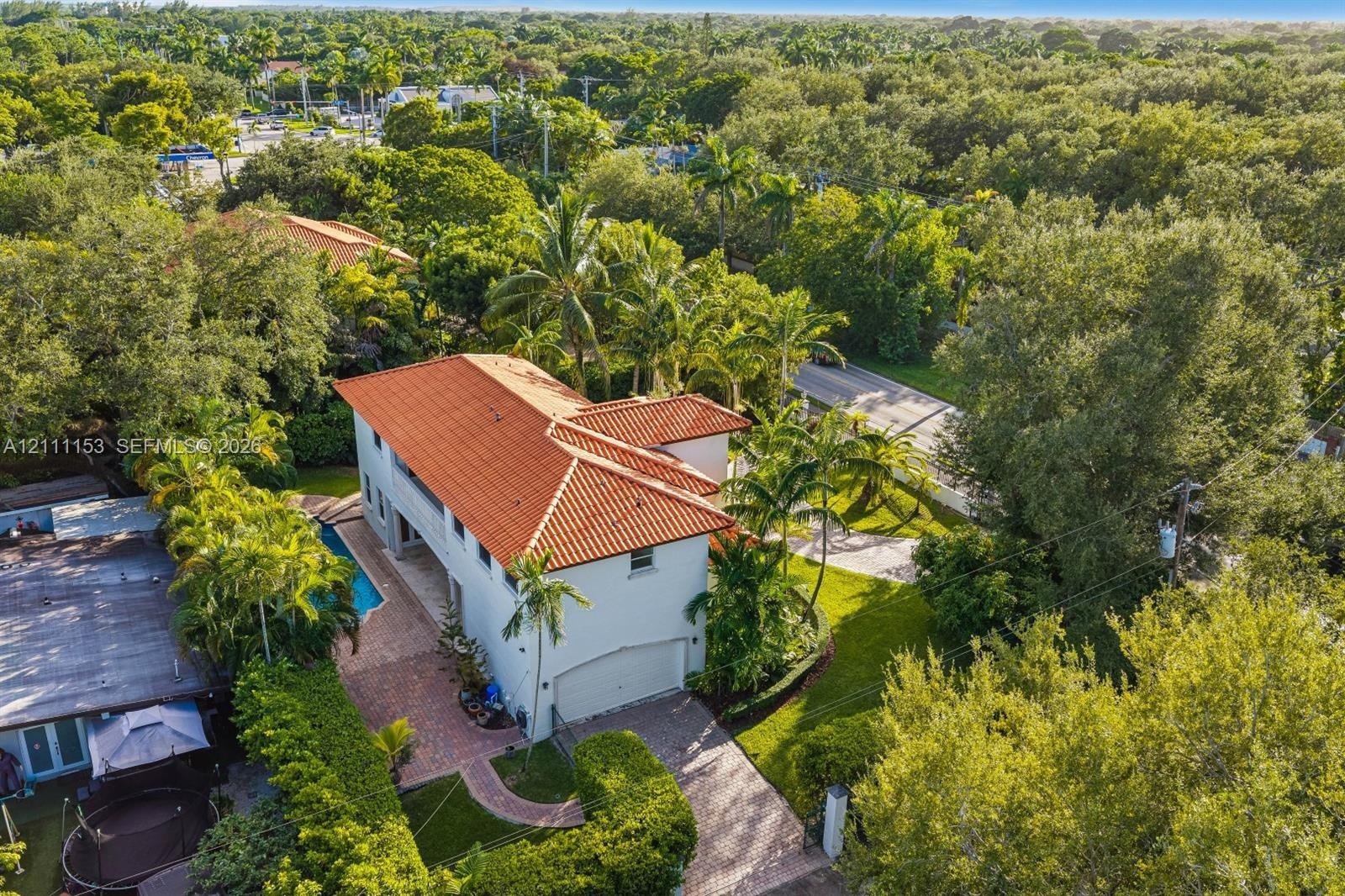 Two-story residence featuring a terracotta-tiled roof, an attached garage, a paved brick driveway, and a swimming pool