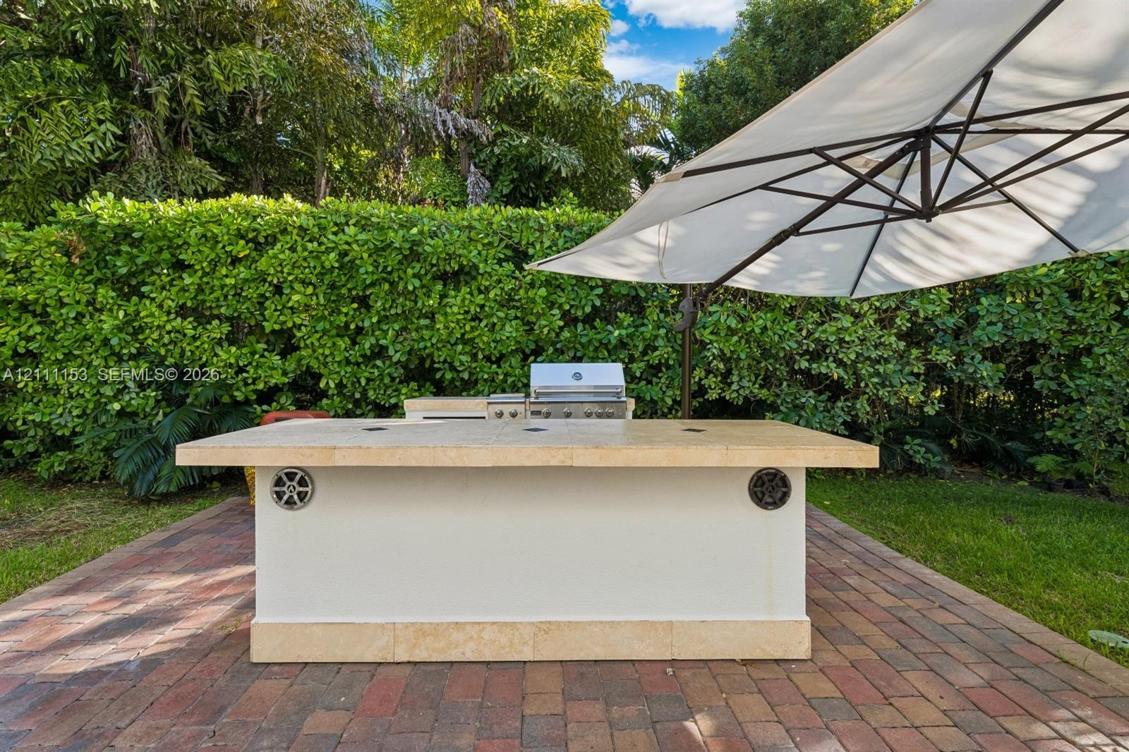 Outdoor kitchen featuring a stone-topped island, stainless steel grill, built-in speakers, and brick paver patio